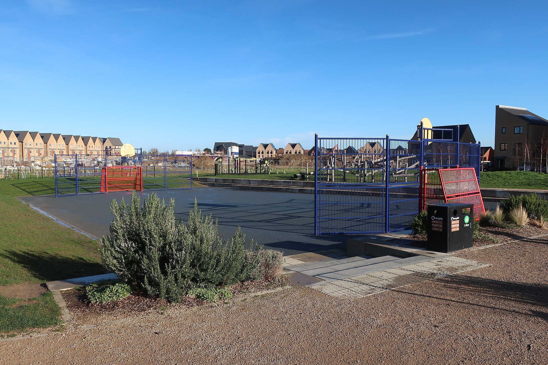 Houses under construction with scaffolding and timber roof trusses, seen across an open grassy field on a new-build housing site.