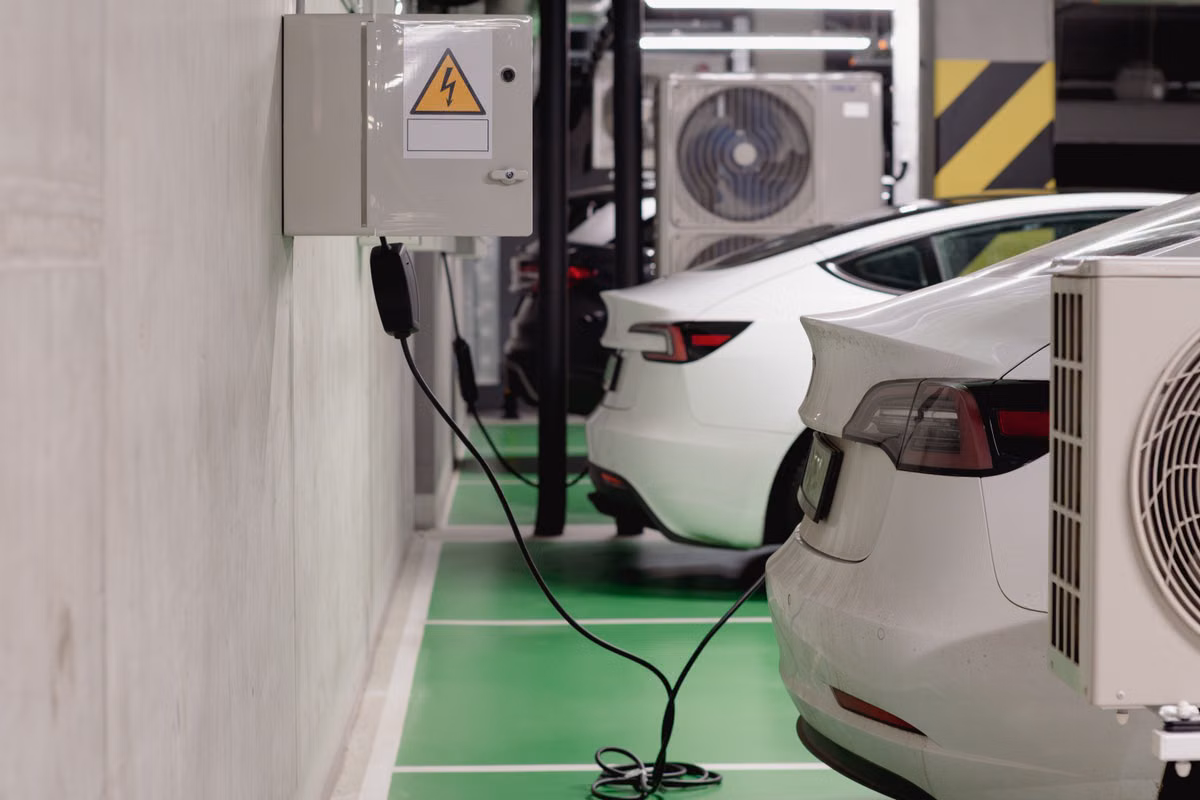 Wall-mounted electric vehicle charge points with cables plugged into parked white cars in an underground car park with green-marked bays.
