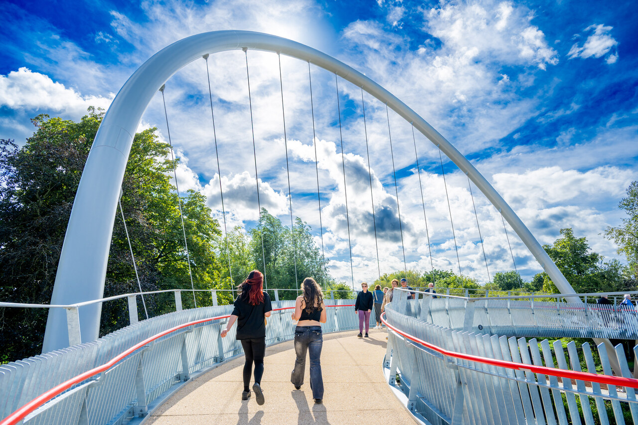 A steel pedestrian and cycle bridge spanning a canal with a towpath alongside